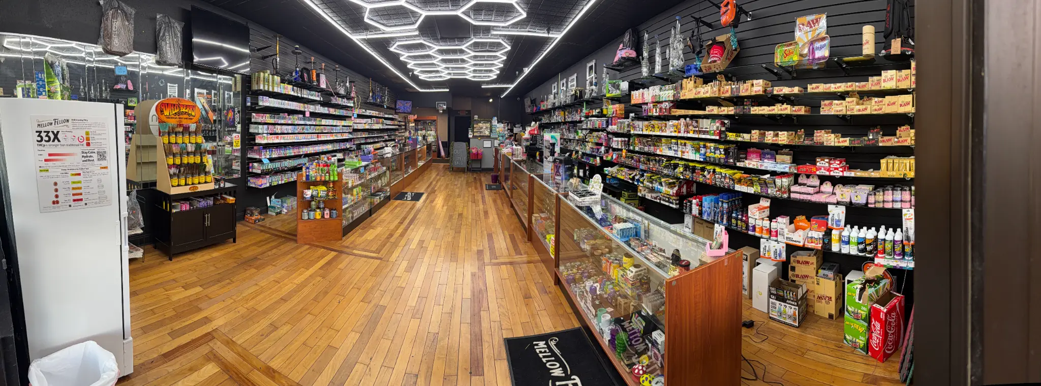 Puffology Smokeshop interior showing hexagonal ceiling lights, extensive vape and glass product displays, and wooden floors in Brandon FL